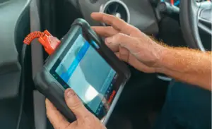 Rapid Truck Repair - Person using a handheld diagnostic tablet mounted in a car interior with an orange coiled cable attached to it