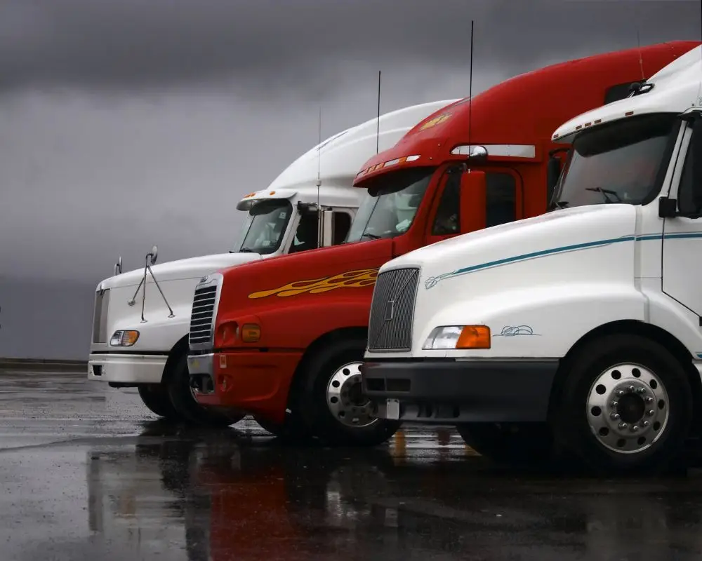 DOT truck inspection San Francisco CA - Rapid Truck Repair - Rapid Truck Repair Rapid Truck Repair - Rapid Truck Repair - Line of white and red semi-trucks parked on a wet tarmac under a cloudy, stormy sky.